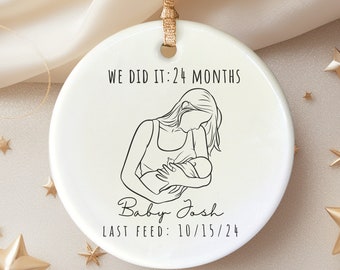 May include: White ceramic ornament with a black line drawing of a mother holding a baby. The text reads "We did it: 24 months Baby Josh Last Feed: 10/15/24"