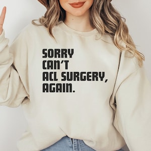 May include: A beige sweatshirt with the text "SORRY CAN'T ACL SURGERY, AGAIN." printed in black.