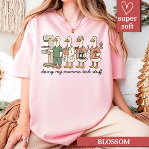 May include: Pink t-shirt with a graphic of four cartoon ducks in medical attire, including a mammogram machine. The text "doing my mammo tech stuff" is below the ducks. The shirt also has the text "super soft" and "BLOSSOM".