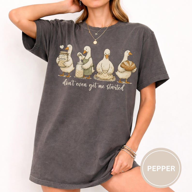 May include: Dark grey t-shirt with a cartoon of four ducks, each with baking items. The text "don't even get me started" is below the ducks. The shirt has a relaxed, oversized fit.