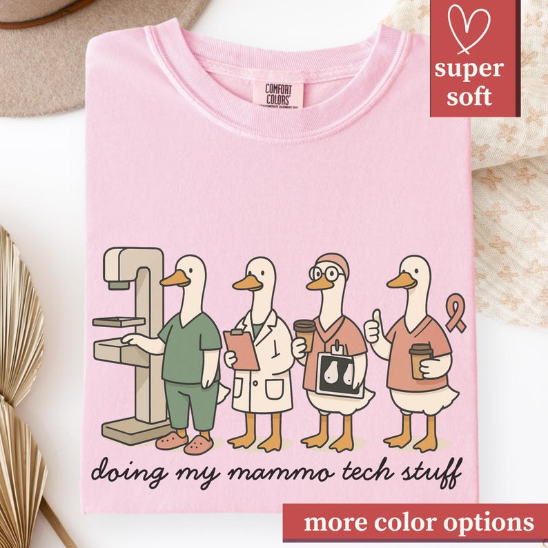 May include: Pink Comfort Colors t-shirt featuring a cartoon of four ducks dressed as mammography technicians. The ducks are depicted with medical equipment and holding coffee cups. The text "doing my mammo tech stuff" is printed below the ducks.