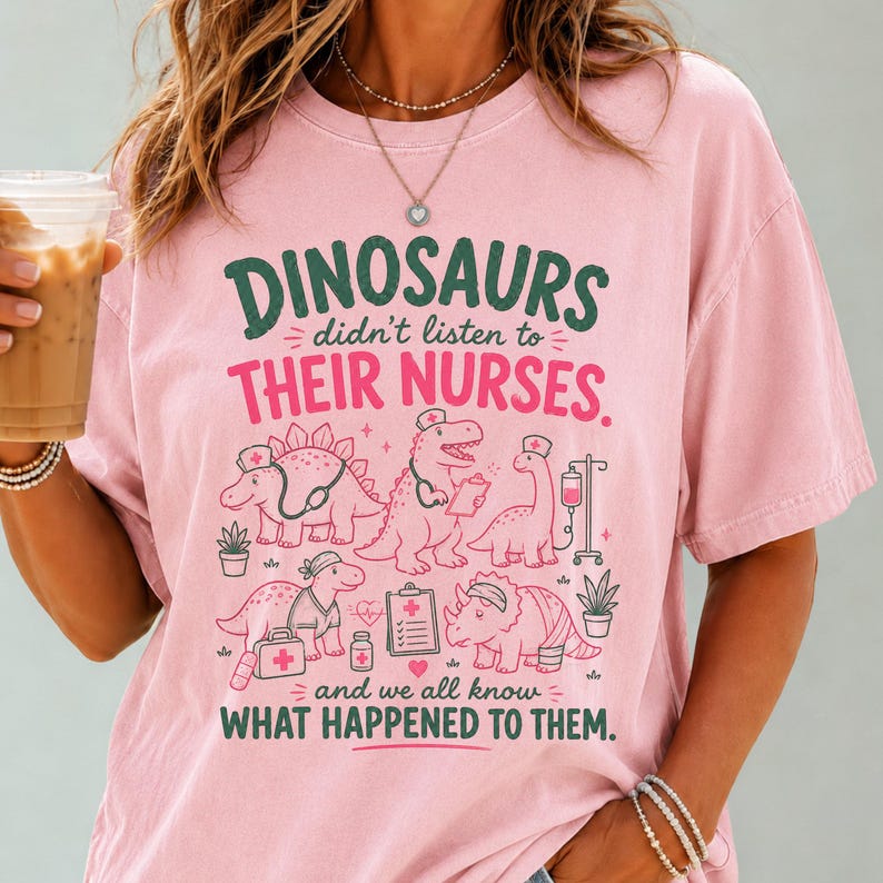 May include: A light pink t-shirt featuring a graphic print of various dinosaurs dressed as nurses with medical equipment. The text reads: DINOSAURS didn't listen to THEIR NURSES. and we all know WHAT HAPPENED TO THEM. The design uses dark green and pink ink.