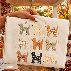 May include: An ivory-colored fabric featuring a repeating pattern of nine stylized dogs in various colors and textures, including floral, plaid, and heart prints, interspersed with small stars, leaves, and swirls across the surface.