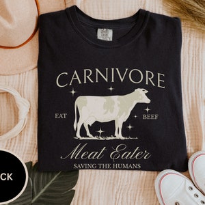 May include: Black t-shirt with a white cow illustration and the text "CARNIVORE EAT BEEF Meat Eater SAVING THE HUMANS".