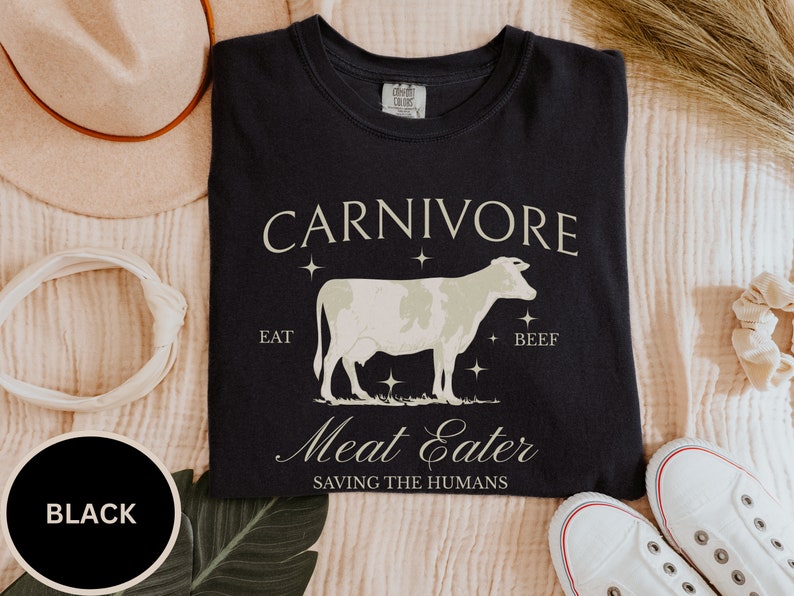 May include: Black t-shirt with a white cow illustration and the text "CARNIVORE EAT BEEF Meat Eater SAVING THE HUMANS".