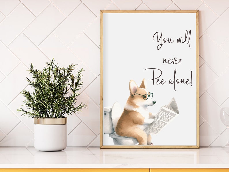 May include: A framed print featuring a watercolor illustration of a Corgi dog wearing glasses and reading a newspaper while sitting on a toilet. The text above the dog reads "You will never Pee alone!"