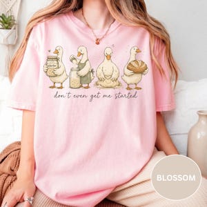 May include: A pale pink t-shirt with a cartoon illustration of four ducks baking, with the words "don't even get me started" underneath. The ducks are shown with baking ingredients and tools.