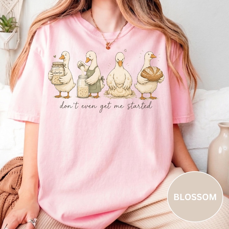 May include: A pale pink t-shirt with a cartoon illustration of four ducks baking, with the words "don't even get me started" underneath. The ducks are shown with baking ingredients and tools.
