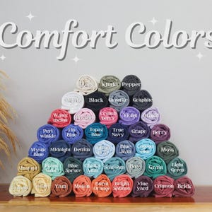 May include: A pyramid of rolled fabric shirts in various colours labelled with text including Ivory, Khaki, Pepper, Black, Granite, Graphite, Watermelon, Blossom, Crunchberry, Violet, Orchid, Periwinkle, Flo Blue, Topaz Blue, True Navy, Grape, Berry, Mystic Blue, Midnight, Denim, Chambray, Blue Jean, Lagoon Blue, Moss, Mustard, Island Reef, Blue Spruce, Chalky Mint, Seafoam, Bay, Grass, Light Green, Banana, Butter, Yam, Melon, Burnt Orange, Bright Salmon, Vineyard, Crimson, and Brick.