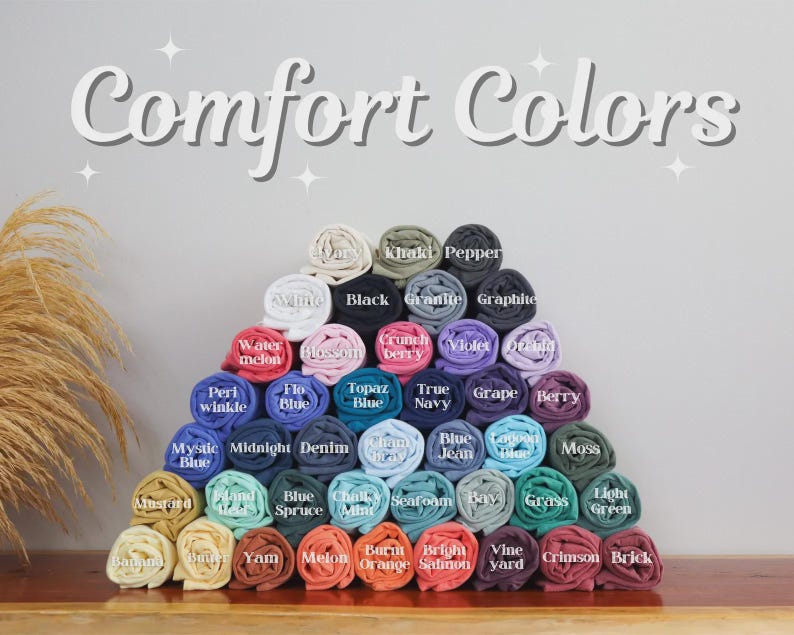 May include: A pyramid of rolled fabric shirts in various colours labelled with text including Ivory, Khaki, Pepper, Black, Granite, Graphite, Watermelon, Blossom, Crunchberry, Violet, Orchid, Periwinkle, Flo Blue, Topaz Blue, True Navy, Grape, Berry, Mystic Blue, Midnight, Denim, Chambray, Blue Jean, Lagoon Blue, Moss, Mustard, Island Reef, Blue Spruce, Chalky Mint, Seafoam, Bay, Grass, Light Green, Banana, Butter, Yam, Melon, Burnt Orange, Bright Salmon, Vineyard, Crimson, and Brick.