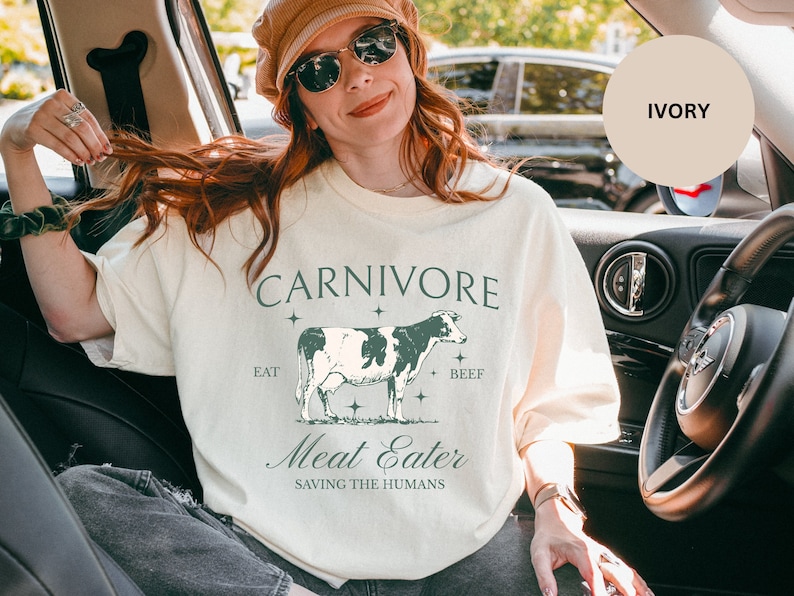 May include: A white t-shirt with a graphic of a cow and the text "CARNIVORE Eat Beef Meat Eater Saving The Humans".