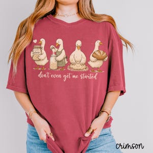 May include: A crimson t-shirt with a humorous design of four white geese involved in baking. The geese are shown with jars, aprons, and a loaf of bread. The text "don't even get me started" is printed below the geese. The word "crimson" is printed on the bottom right.