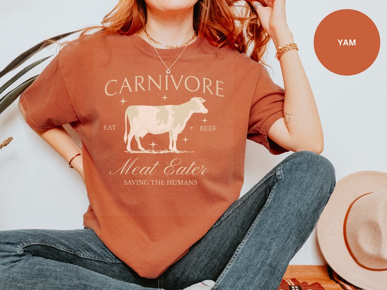 May include: A rust-colored t-shirt with a white cow graphic and the text "CARNIVORE EAT BEEF Meat Eater SAVING THE HUMANS".