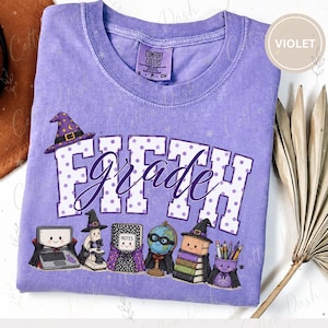 May include: A violet short-sleeve t-shirt featuring the text FIFTH grade in white with purple polka dots. The design includes cartoon illustrations of a laptop, microscope, notebook, globe, books, and pencils, all wearing witch hats and capes.