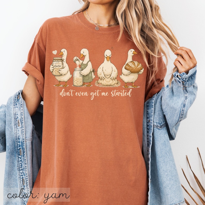 May include: A yam-coloured t-shirt with a whimsical illustration of four ducks involved in baking. The ducks are depicted with jars, aprons, and a loaf of bread, with the phrase "don't even get me started" below.