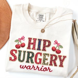 以下が含まれることがあります： クリーム色のTシャツ。パッチワークデザインで「HIP SURGERY warrior」の文字。ピンクのリボンが付いたチェリーのグラフィックが特徴。ペンダント付きのゴールドネックレスがTシャツにかけられています。