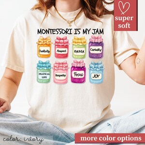 May include: Ivory-colored t-shirt with the text "MONTESSORI IS MY JAM" and colorful jam jar graphics. Each jar has a different word: Creativity, Respect, Order, Curiosity, Practical Life, Empathy, Focus, and Joy.