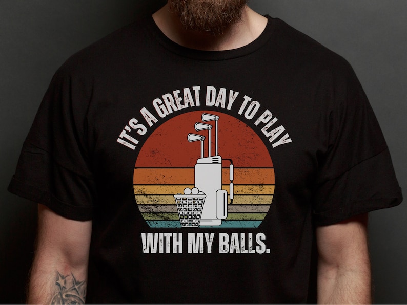 May include: A black t-shirt with a vintage-style graphic of a golf bag with clubs and golf balls. The text reads "It's a great day to play with my balls."