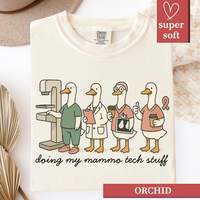 May include: Cream-colored t-shirt featuring a cartoon of four ducks in medical attire, including a mammogram machine. The text "doing my mammo tech stuff" is below the ducks. The shirt also has the word "ORCHID" at the bottom.