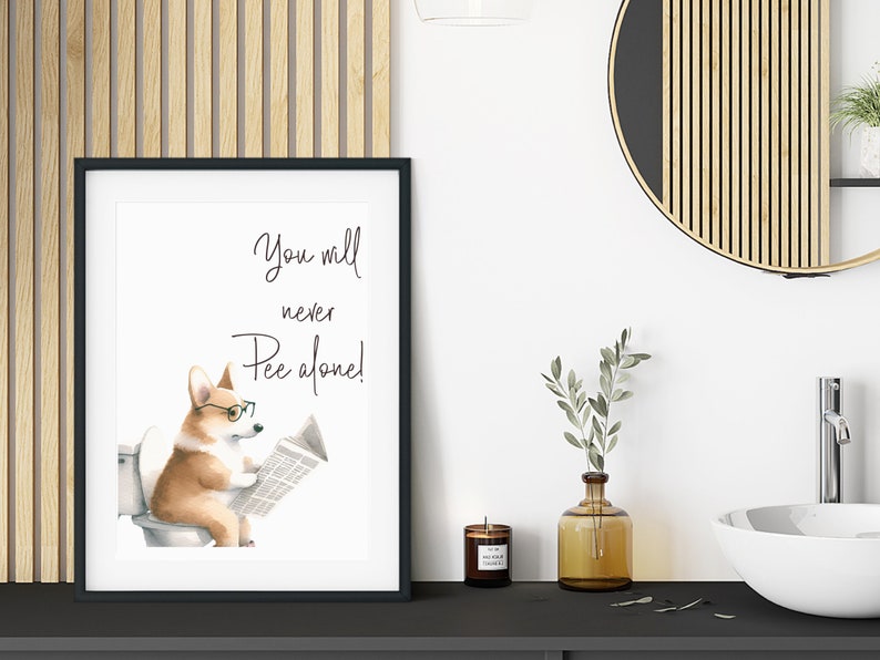 May include: Framed art print featuring a watercolor illustration of a corgi wearing glasses and reading a newspaper while sitting on a toilet. The text above the corgi reads, "You will never Pee alone!" The print is in a black frame.