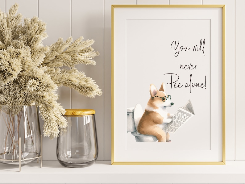 May include: A framed print with a gold border features a watercolor illustration of a corgi wearing glasses and reading a newspaper while sitting on a toilet. The text above the corgi reads, "You will never Pee alone!"