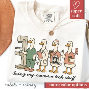 May include: Ivory-colored t-shirt featuring a cartoon of four ducks in medical attire, with a mammogram machine. The text "doing my mammo tech stuff" is printed below the ducks. The shirt has a round neckline and short sleeves.