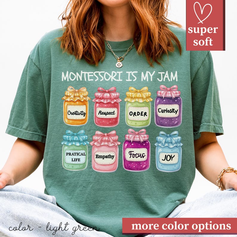 May include: Light green t-shirt with the text "MONTESSORI IS MY JAM" and illustrations of jam jars labeled with words like "Creativity" and "Joy." The shirt has a "super soft" label.