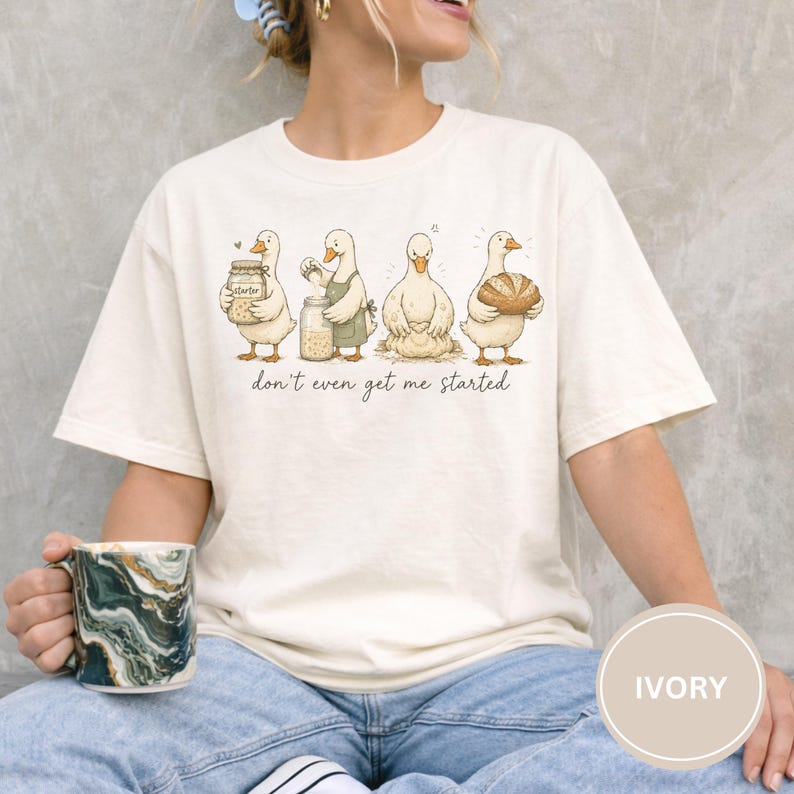 May include: Cream-coloured t-shirt with a cartoon illustration of four ducks preparing food. The ducks are shown with jars, aprons, and bread. The text "don't even get me started" is printed below the ducks.