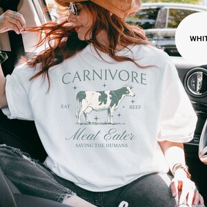 May include: White t-shirt with a graphic of a cow and the text "CARNIVORE", "EAT", "BEEF", "Meat Eater", and "SAVING THE HUMANS".