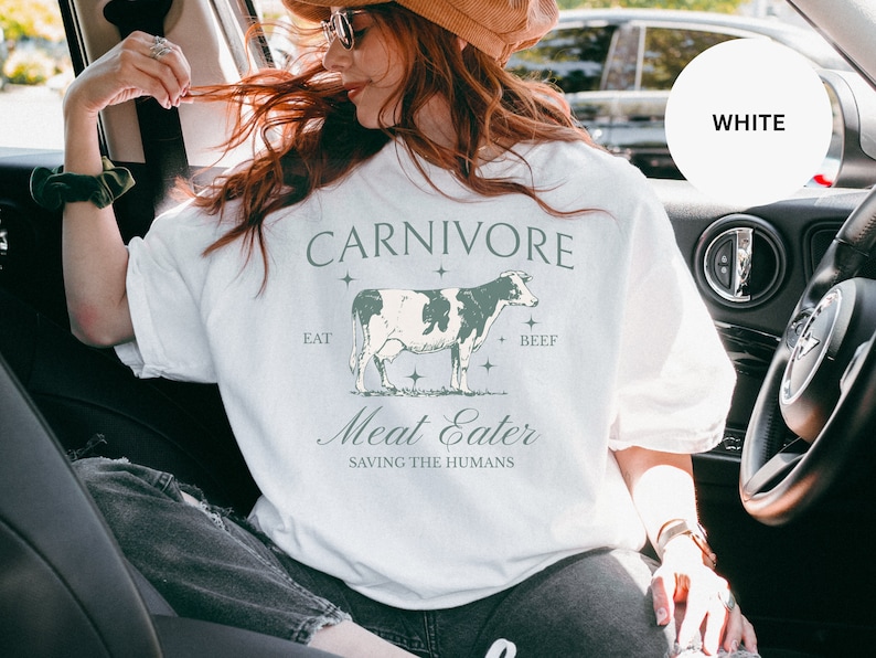 May include: White t-shirt with a graphic of a cow and the text "CARNIVORE", "EAT", "BEEF", "Meat Eater", and "SAVING THE HUMANS".