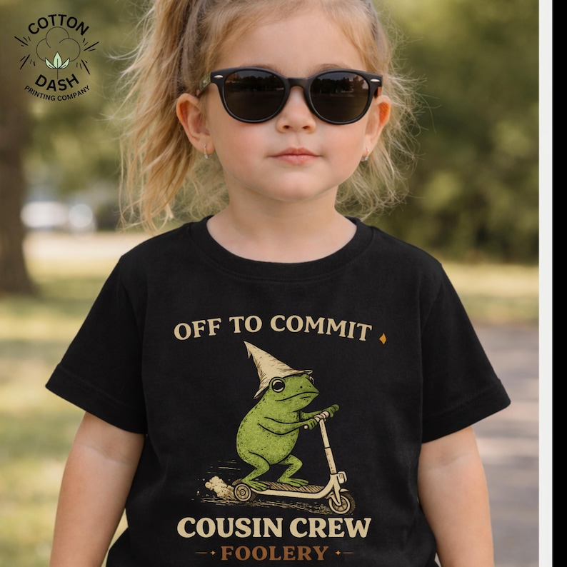 K&ouml;nnte beinhalten: Schwarzes T-Shirt mit dem Text "OFF TO COMMIT" &uuml;ber einem gr&uuml;nen Frosch auf einem Roller. Der Frosch tr&auml;gt einen spitzen Hut und der Text "COUSIN CREW - FOOLERY" steht darunter. Das Shirt stammt von Cotton Dash Printing Company.