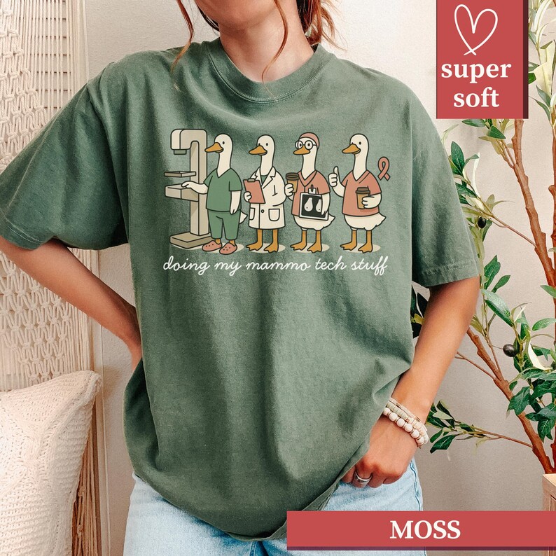 May include: Moss green t-shirt featuring a cartoon illustration of four ducks in medical attire, including a mammogram machine. The text "doing my mammo tech stuff" is below the illustration. The shirt has a "super soft" label.