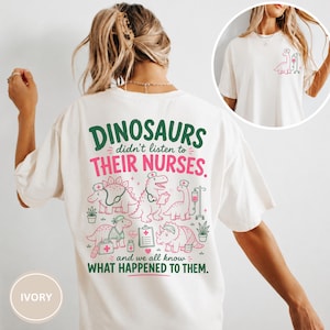 May include: An ivory t-shirt featuring a graphic on the back with green and pink text that reads: DINOSAURS didn't listen to THEIR NURSES. and we all know WHAT HAPPENED TO THEM. The design includes illustrations of dinosaurs wearing nurse caps.