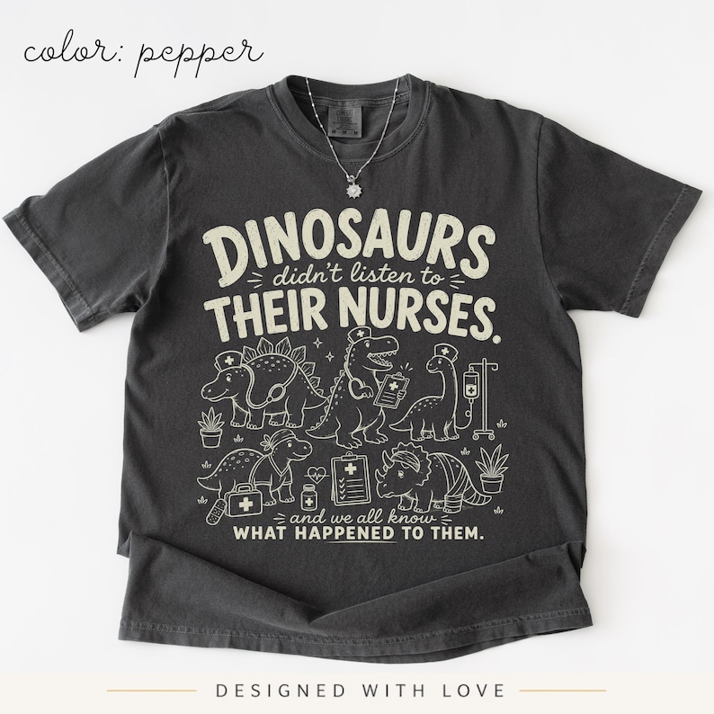 May include: A pepper-colored t-shirt featuring a graphic print with the text "DINOSAURS didn't listen to THEIR NURSES. and we all know WHAT HAPPENED TO THEM." The design includes illustrations of dinosaurs wearing nurse caps and medical gear.