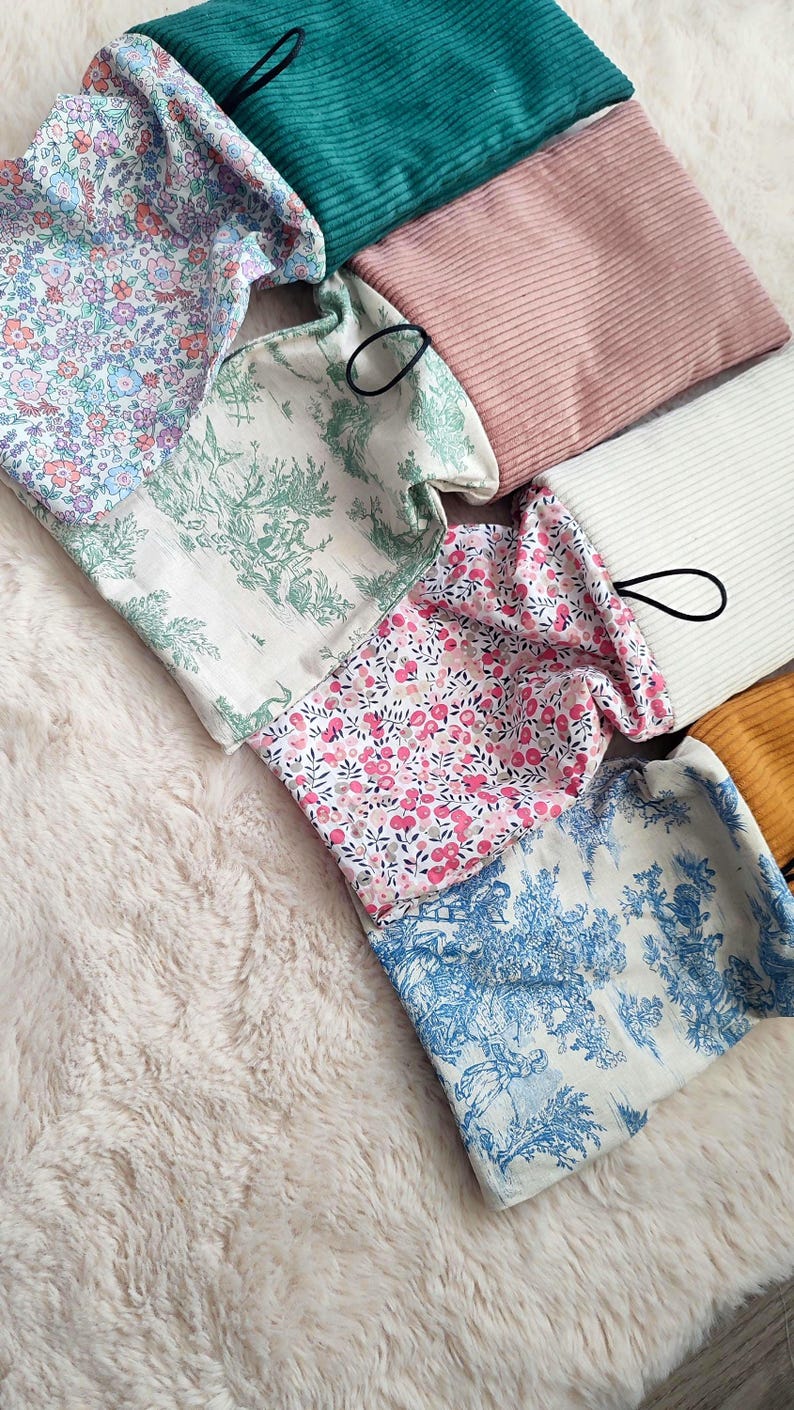 May include: An assortment of fabric pouches in various colors and patterns. The pouches include floral prints in pink and blue, a toile design, and solid colors like teal, pink, and gold. Each pouch has a black loop attached.