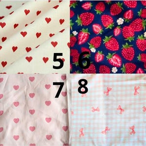 May include: Fabric swatches with various patterns. One swatch features red hearts on a cream background. Another displays strawberries and white flowers on a navy blue background. Other swatches have pink hearts and bows.