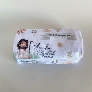 Pu&ograve; includere: Coperta di peluche bianca con un motivo floreale e un'immagine di un pastore in stile cartone animato. La coperta ha il testo "St. Elizabeth pray for me" e "Amelia Elizabeth 04.07.24" stampato su di essa.