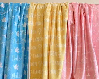 May include: Three fleece blankets with different patterns and colours. The first blanket is light blue with white doves and the name Mateo repeated. The second blanket is yellow with white text that says Landon repeated. The third blanket is pink with white crosses and the name Isabella repeated.