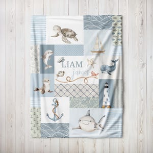 May include: A blue and white baby blanket with a patchwork design featuring sea creatures, a lighthouse, an anchor, and the names Liam James.