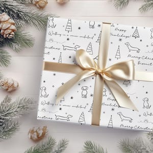 May include: White gift wrap with a black and white pattern of dogs, Christmas trees, and stars. The text "Happy Howlidays!" and "Walking in a winter wonderland" are repeated throughout the pattern. The gift wrap is tied with a gold ribbon.