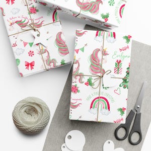 May include: White wrapping paper with a repeating pattern of pink and green unicorns, rainbows, candy canes, and holly. The text "Have a Magical Christmas" and "I believe in Santa and unicorns" are printed on the paper. The paper is wrapped around a gift box with a white tag.