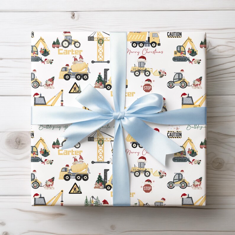 May include: White wrapping paper with a repeating pattern of construction vehicles, Christmas trees, and the name "Carter". The vehicles are yellow and red, and the trees are green. The text "Merry Christmas" and "Caution" are also included in the pattern.