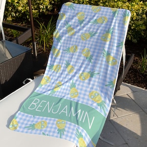 May include: A blue and white gingham beach towel with a pineapple pattern and the name "BENJAMIN" printed on a green stripe.
