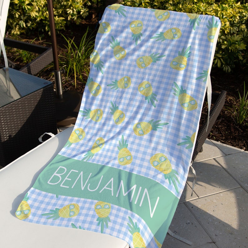 May include: A blue and white gingham beach towel with a pineapple pattern and the name "BENJAMIN" printed on a green stripe.