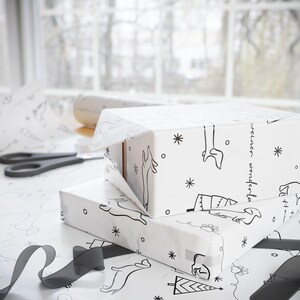 May include: Two white gift boxes wrapped in black and white patterned paper with a reindeer and tree design. The paper has the text "weiner wonderland" printed on it. The boxes are stacked on top of each other.