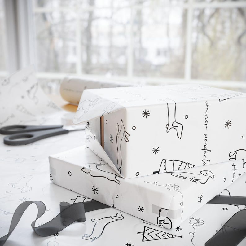 May include: Two white gift boxes wrapped in black and white patterned paper with a reindeer and tree design. The paper has the text "weiner wonderland" printed on it. The boxes are stacked on top of each other.