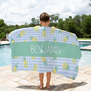 May include: A blue and white gingham beach towel with a pineapple pattern and the name "BENJAMIN" printed in white on a green stripe.