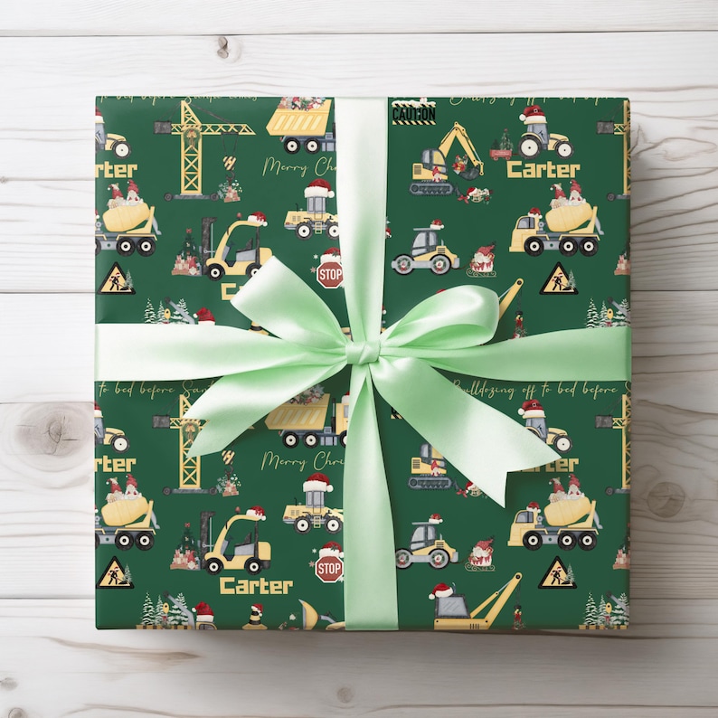 May include: Green wrapping paper with a repeating pattern of construction vehicles, including a crane, dumper truck, cement mixer, and bulldozer. The paper also features a Christmas tree, a stop sign, and the words "Merry Christmas" and "Carter".