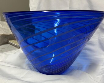 Può includere: Una ciotola di vetro blu vibrante con una forma conica. La ciotola presenta una serie di strisce diagonali blu più chiare. Il vetro è trasparente, consentendo il passaggio della luce. Questa ciotola decorativa è adatta per l'arredamento della casa.