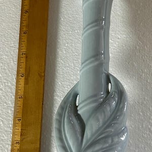 May include: A light blue ceramic lamp base with a decorative leaf design. The lamp base has a spiral design on the stem and measures approximately 12 inches tall. The lamp has a silver lamp socket.